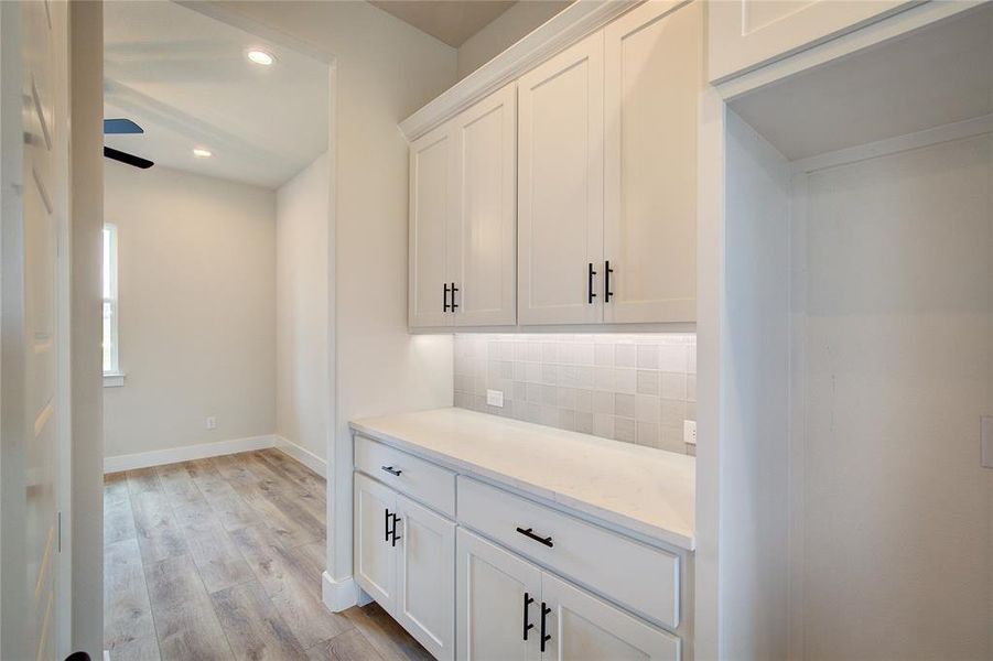 Kitchen with light hardwood / wood-style floors, tasteful backsplash, white cabinetry, and ceiling fan