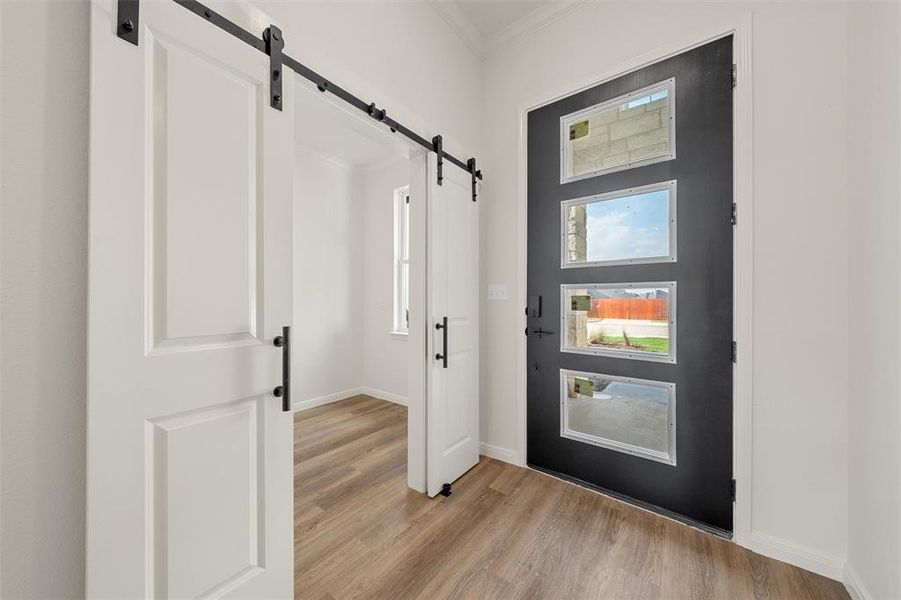 Foyer entrance featuring a barn door, ornamental molding, and light wood finished floors Foyer entrance featuring a barn door, ornamental molding, and light wood finished floors