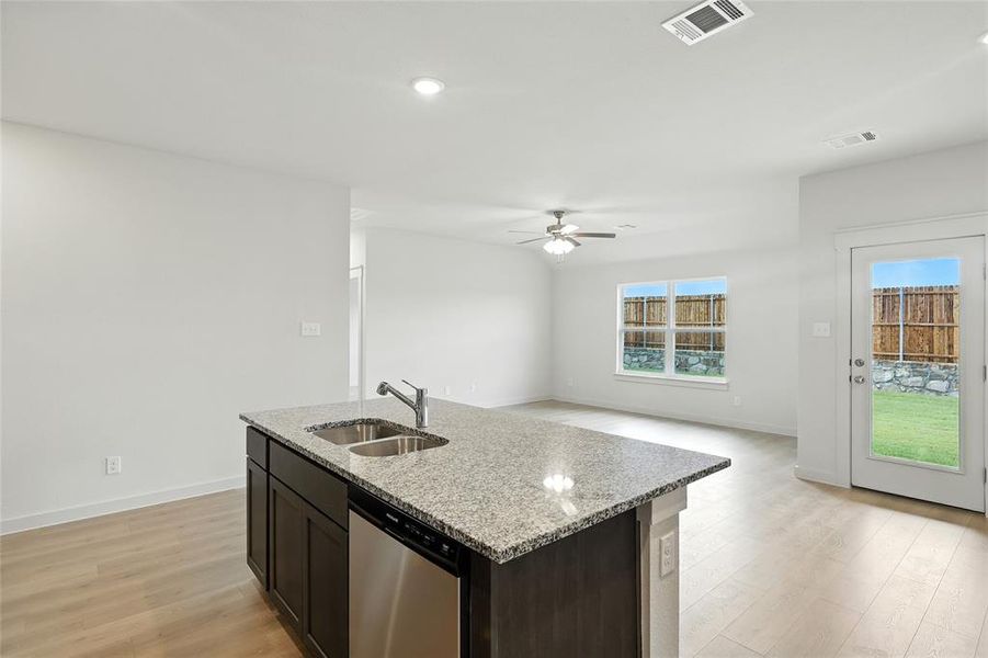 Kitchen with light wood finished floors, light stone counters, dishwasher, an island with sink, and dark brown cabinetry Kitchen with light wood finished floors, light stone counters, dishwasher, an island with sink, and dark brown cabinetry