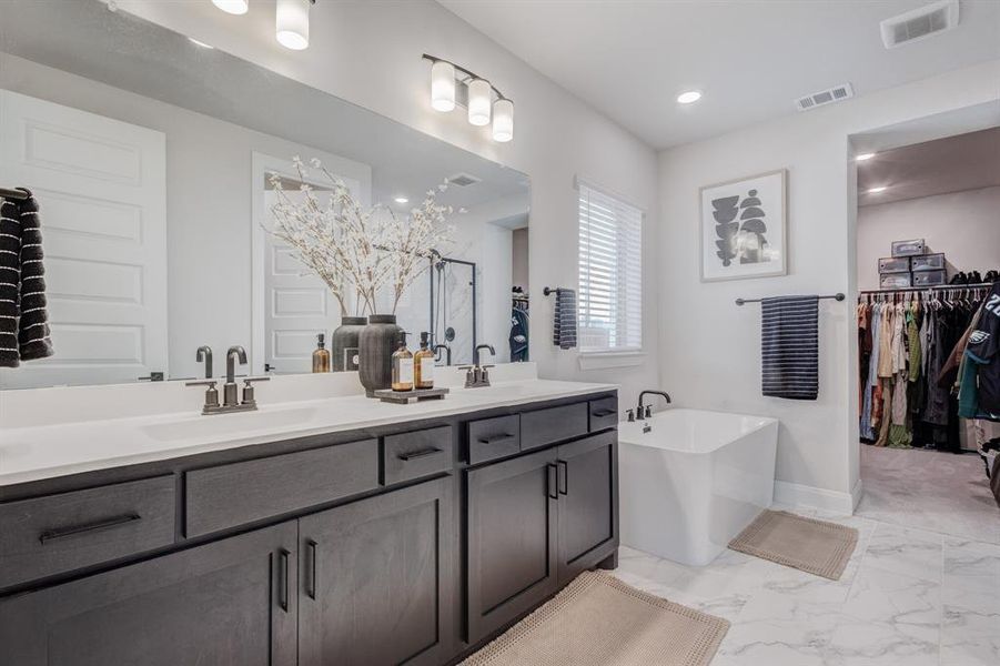 Bathroom with a soaking tub, a walk in closet, double vanity, and light marble finish floors
