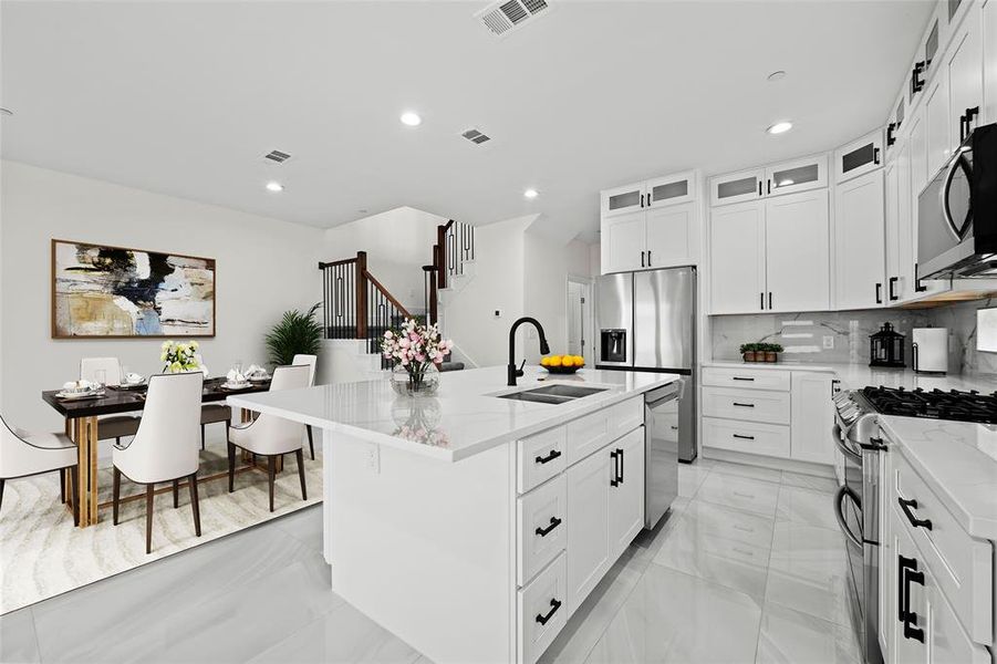 Kitchen with an island with sink, backsplash, light stone countertops, stainless steel appliances, and sink