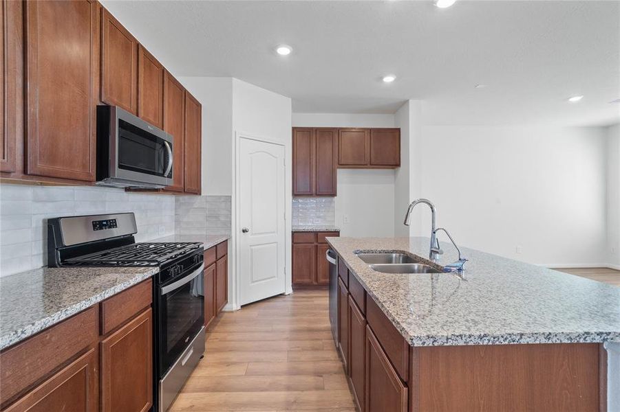 This spacious kitchen features high ceilings, recessed lighting, stained wood cabinets, granite countertops, SS appliances, modern tile backsplash, huge granite kitchen island with large sink and space for breakfast bar, and a pantry all overlooking your huge family room.