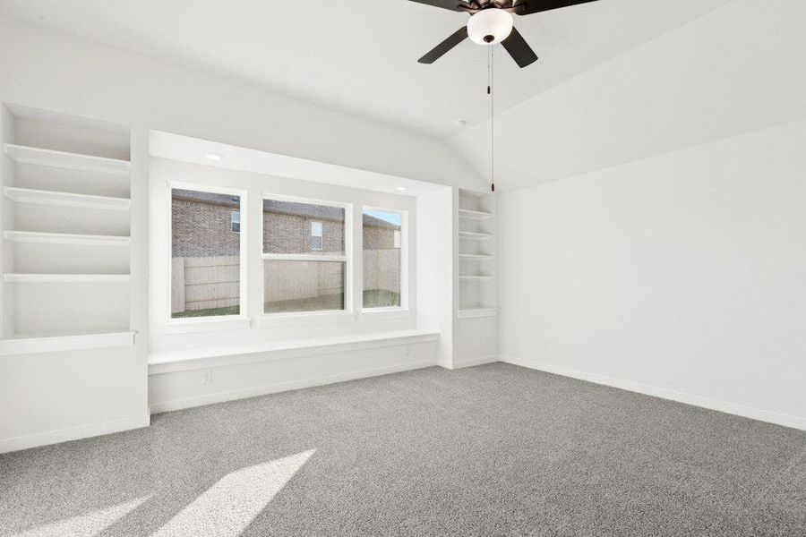 Carpeted spare room featuring built in shelves, vaulted ceiling, and a ceiling fan Carpeted spare room featuring built in shelves, vaulted ceiling, and a ceiling fan
