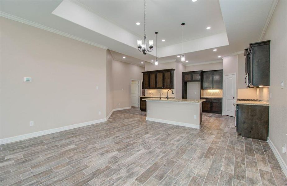 This is a spacious open-concept living area with tiled flooring, featuring a modern kitchen with dark cabinetry, a central island, and elegant lighting fixtures.