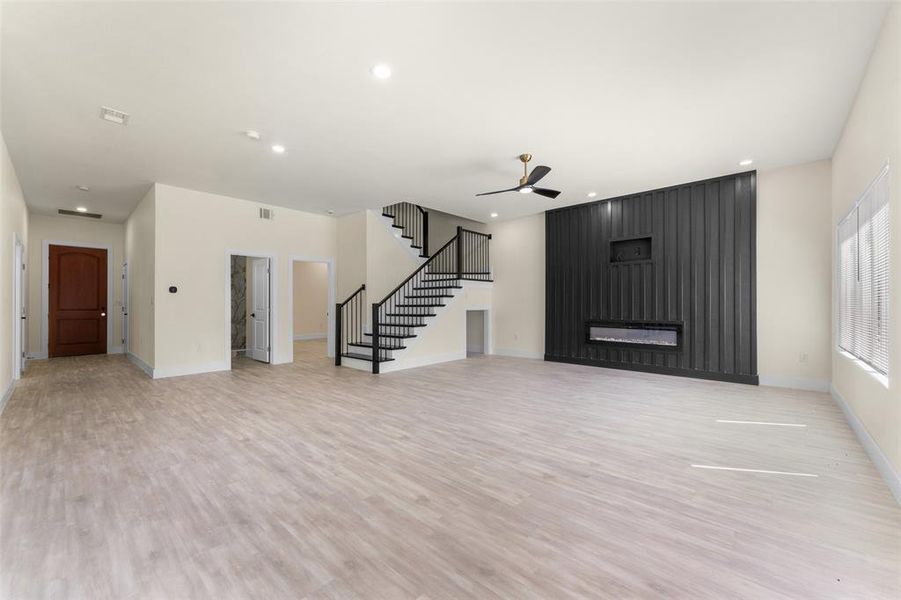Unfurnished living room with a ceiling fan, stairway, light wood-style floors, recessed lighting, and a large fireplace