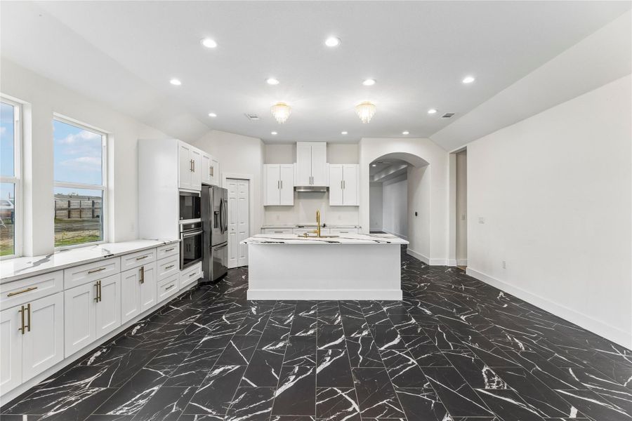 A contemporary kitchen features sleek white cabinetry and a striking black and white marble-look floor.