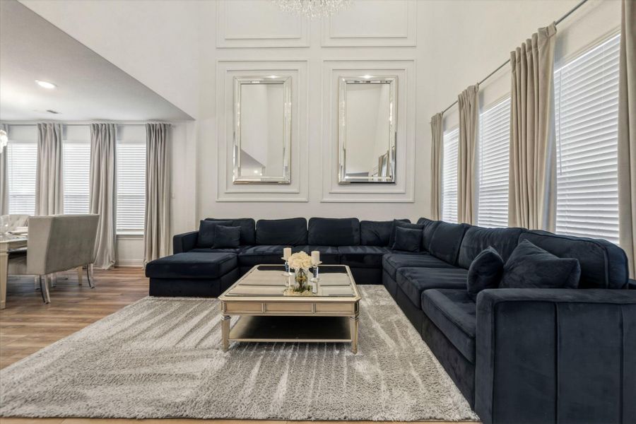 Spacious living area featuring high ceilings with intricate wall molding, and multiple large windows with blinds