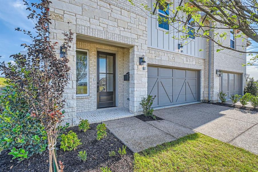 Doorway to property featuring driveway, stone siding, an attached garage, and board and batten siding