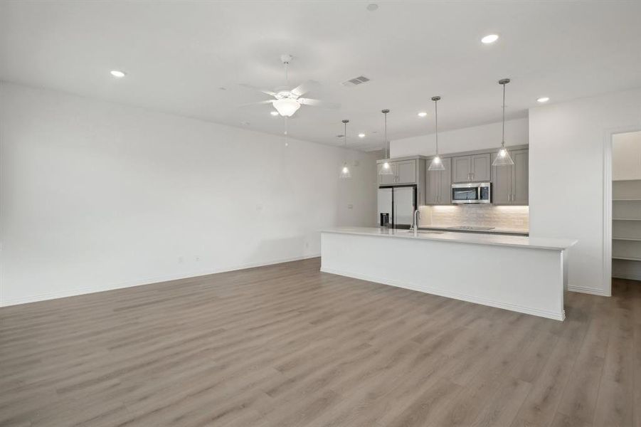 Kitchen with stainless steel appliances, decorative light fixtures, gray cabinets, a kitchen island with sink, and hardwood / wood-style flooring