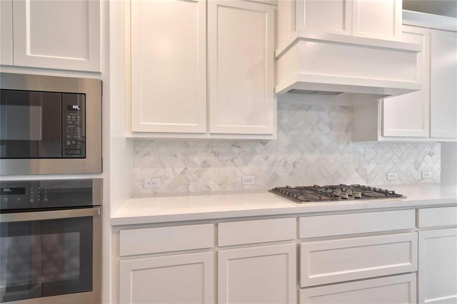 Kitchen featuring stainless steel appliances, white cabinetry, and tasteful backsplash