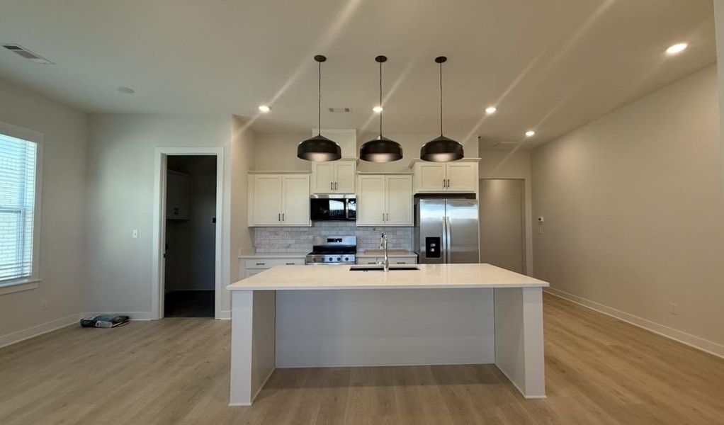 Kitchen with stainless steel appliances, a center island with sink, white cabinets, and light wood-style flooring