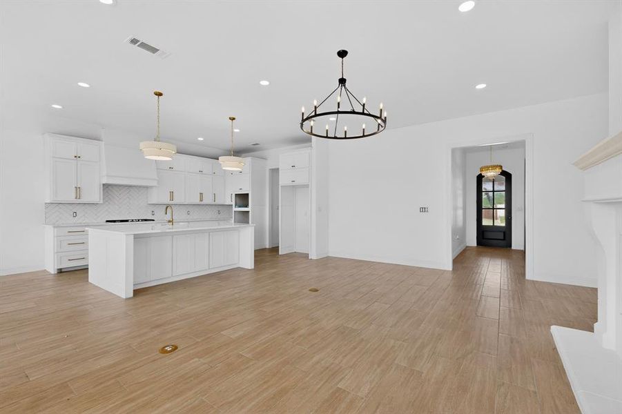 Open concept living space featuring wood-finish flooring, a white kitchen with a center island and pendant lighting, and a white fireplace mantel Open concept living space featuring wood-finish flooring, a white kitchen with a center island and pendant lighting, and a white fireplace mantel