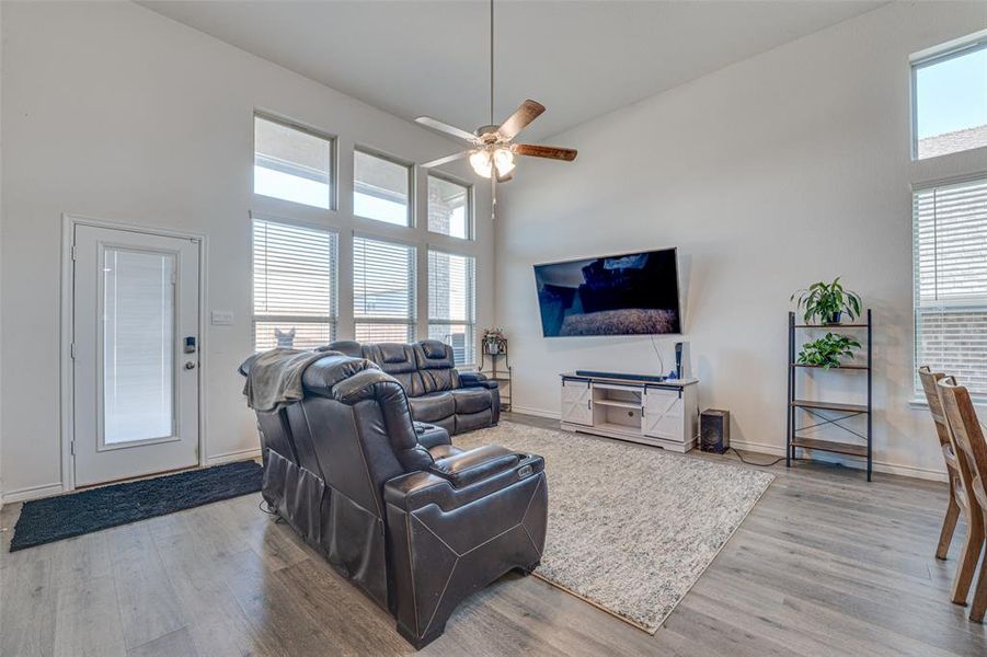 Living room with a towering ceiling, light wood finished floors, and ceiling fan