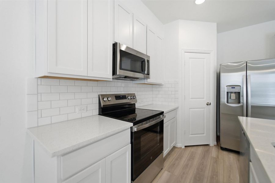 Kitchen featuring stainless steel appliances, light wood-style flooring, white cabinets, and backsplash Kitchen featuring stainless steel appliances, light wood-style flooring, white cabinets, and backsplash