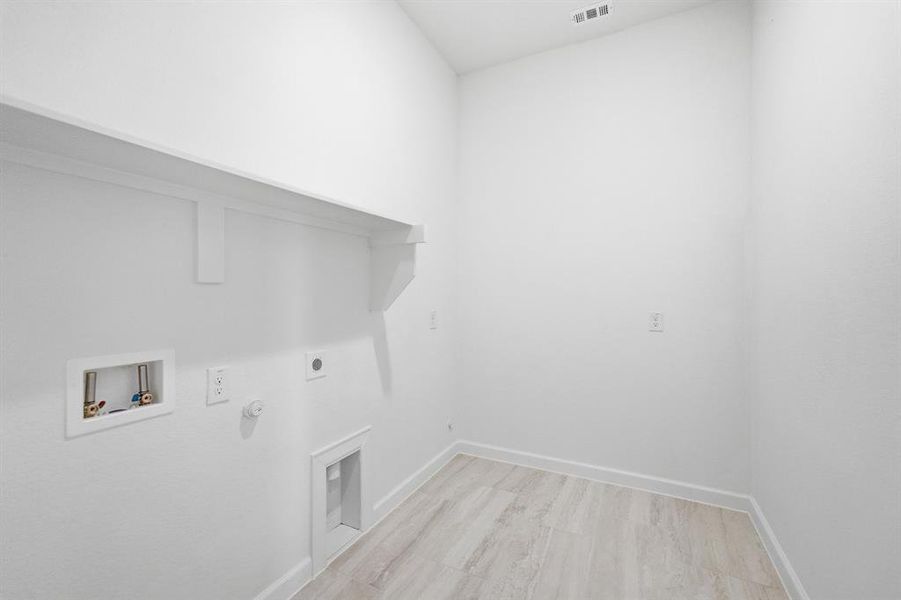Dedicated laundry area featuring a built-in shelf, appliance hookups, and light wood-finish flooring Dedicated laundry area featuring a built-in shelf, appliance hookups, and light wood-finish flooring