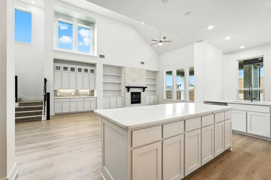 Kitchen featuring a center island, a fireplace, high vaulted ceiling, white cabinetry, and light wood-style flooring Kitchen featuring a center island, a fireplace, high vaulted ceiling, white cabinetry, and light wood-style flooring
