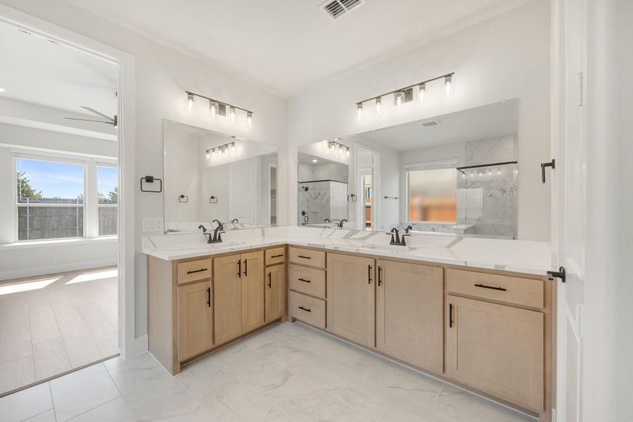 Master bathroom with dual sinks, light wood L-shaped vanity, white countertops, and large mirrors with modern lighting. Master bathroom with dual sinks, light wood L-shaped vanity, white countertops, and large mirrors with modern lighting.