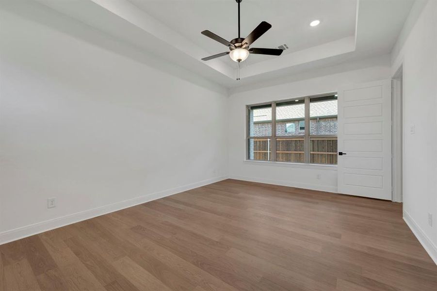 Empty room with dark wood-style flooring, ceiling fan, and a raised ceiling