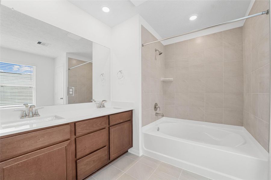 This move-in ready primary bathroom offers a spacious tub/shower combination with a tiled surround, stained cabinetry topped with light countertops, dual sinks, high ceilings, neutral paint, a large mirror, and sleek, modern finishes for a polished look. This move-in ready primary bathroom offers a spacious tub/shower combination with a tiled surround, stained cabinetry topped with light countertops, dual sinks, high ceilings, neutral paint, a large mirror, and sleek, modern finishes for a polished look.
