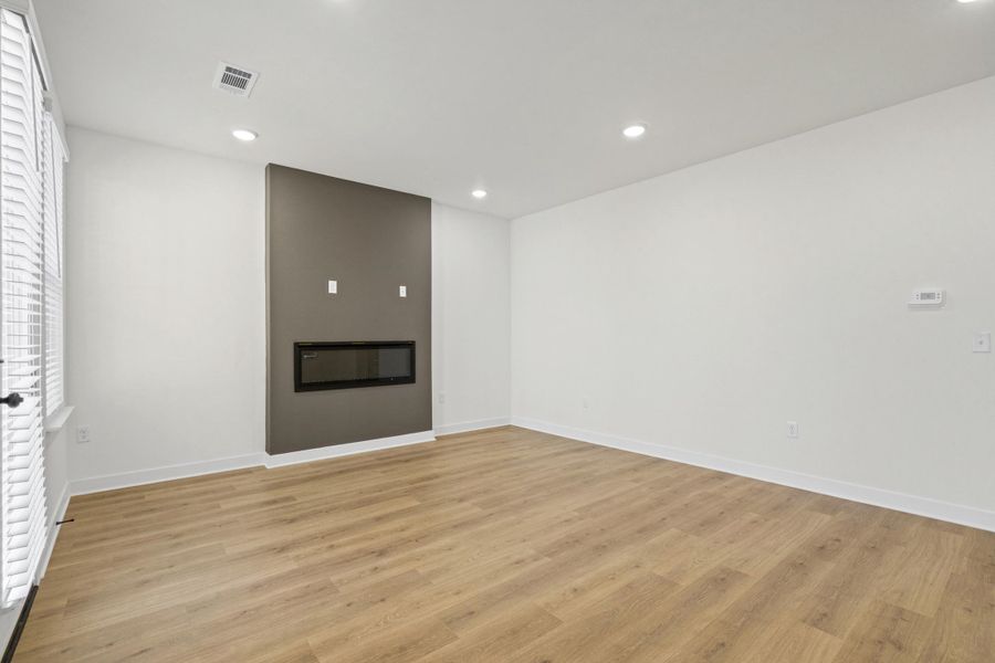 Spacious room featuring wood-finish flooring, a contemporary linear fireplace on an accent wall, recessed lighting, and a window with blinds