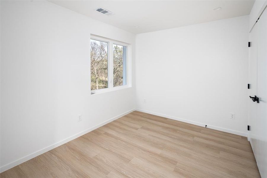 Empty room with baseboards, light wood finished floors, and visible vents