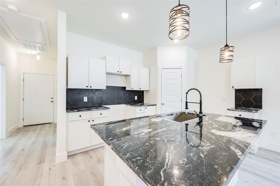 Kitchen with backsplash, dark stone counters, white cabinetry, light wood-style flooring, and hanging light fixtures