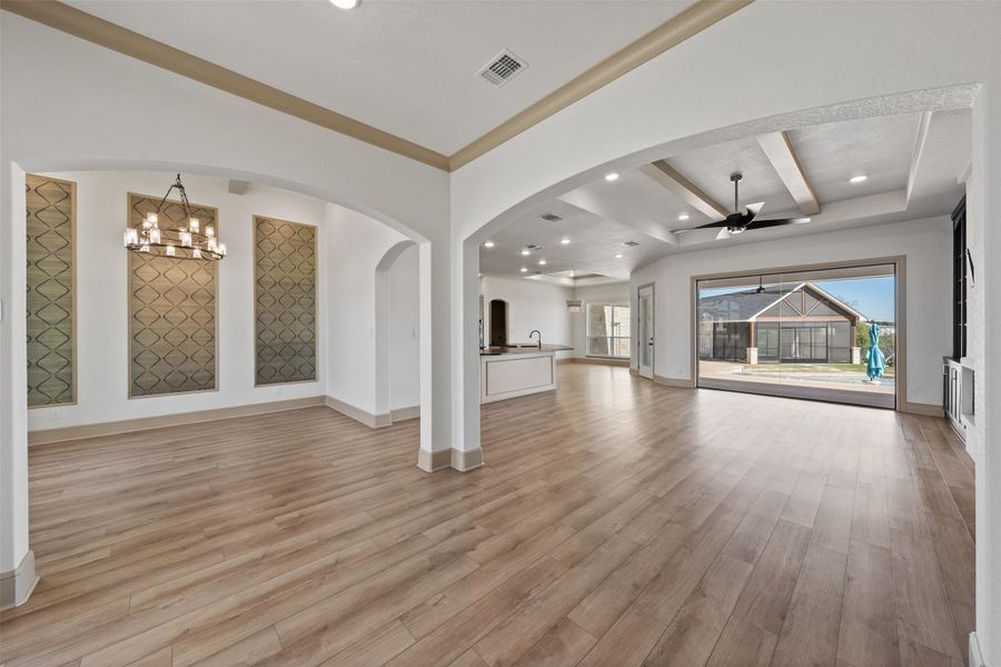 Unfurnished living room featuring visible vents, light wood-style flooring, ceiling fan with notable chandelier, arched walkways, and baseboards