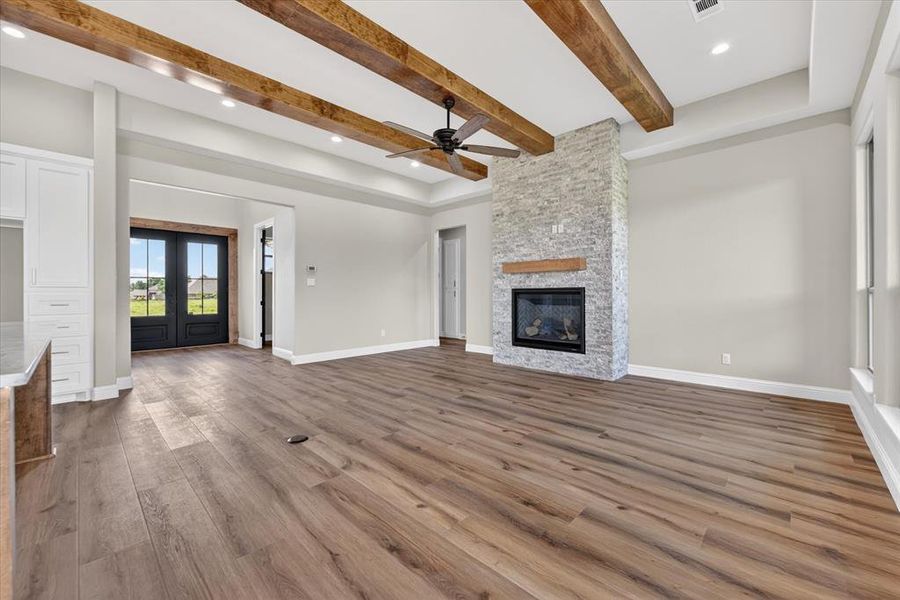 Spacious open-concept room featuring wood-finish flooring, a stone-clad fireplace with a wood mantel, exposed ceiling beams, and recessed lighting