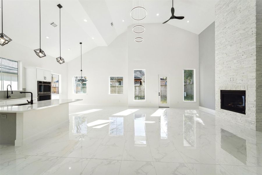 Stunning modern open-concept living space featuring soaring ceilings, sleek marble-style flooring, designer lighting, and beautiful windows filling the home with natural light.