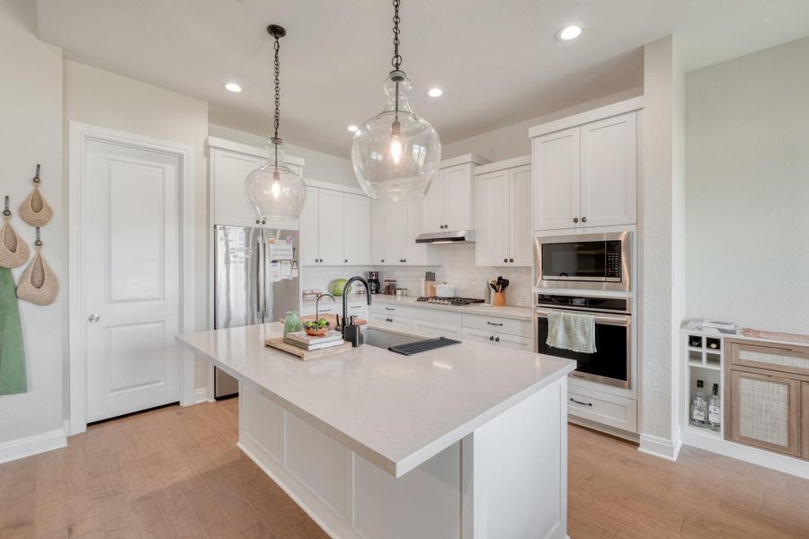 The kitchen is crisp and bright with quartz countertops, SS appliances, glass pendant lighting, and an oversized island.