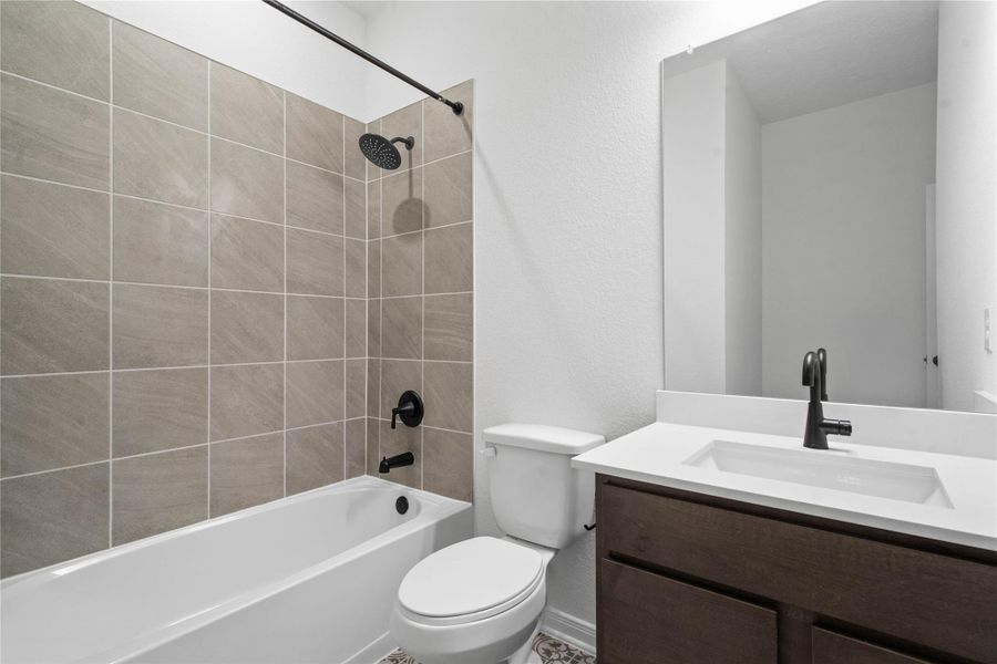 The secondary bathroom showcases tile flooring, a bath/shower combo with Daltile tile surround, a vanity with stunning light countertop, a mirror, sleek fixtures, and contemporary finishes throughout.
