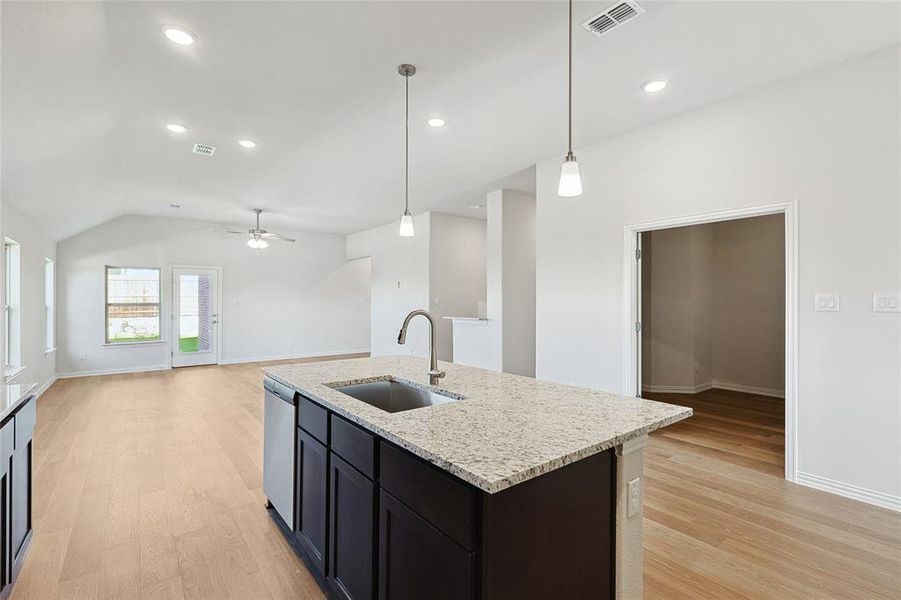 Kitchen with stainless steel dishwasher, ceiling fan, sink, light stone counters, and light hardwood / wood-style flooring