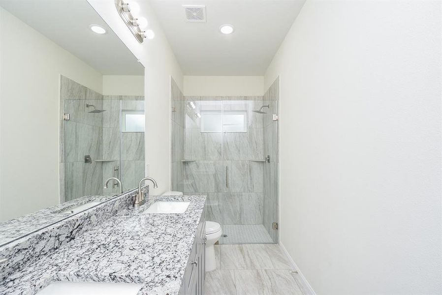 Modern bathroom with a large mirror, granite countertop, undermount sink, glass shower, and white toilet. Clean, bright, and minimalistic design.