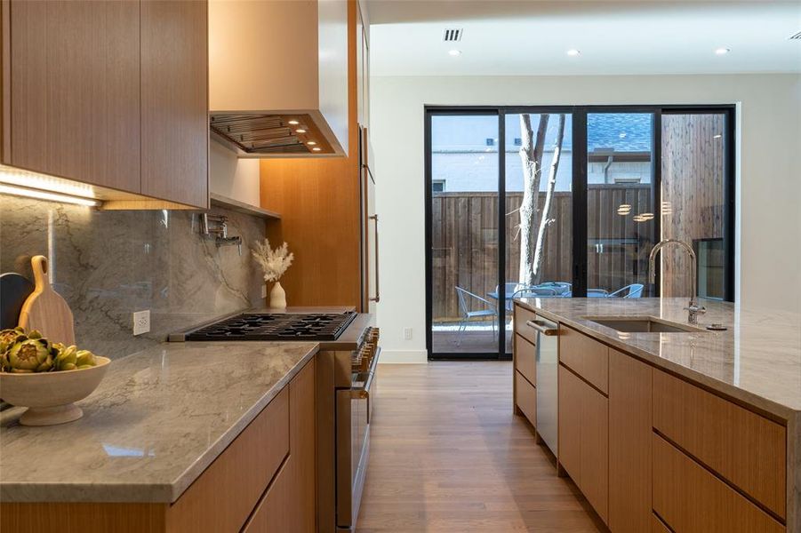 Kitchen featuring sink, range hood, stainless steel appliances, light stone counters, and light hardwood / wood-style floors