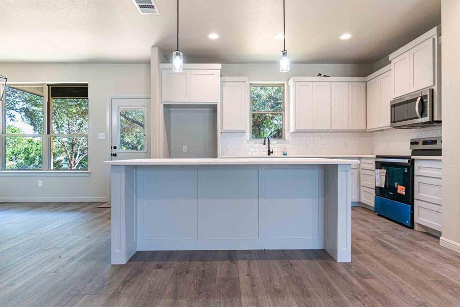 Kitchen with stainless steel appliances, tasteful backsplash, hanging light fixtures, recessed lighting, and a center island