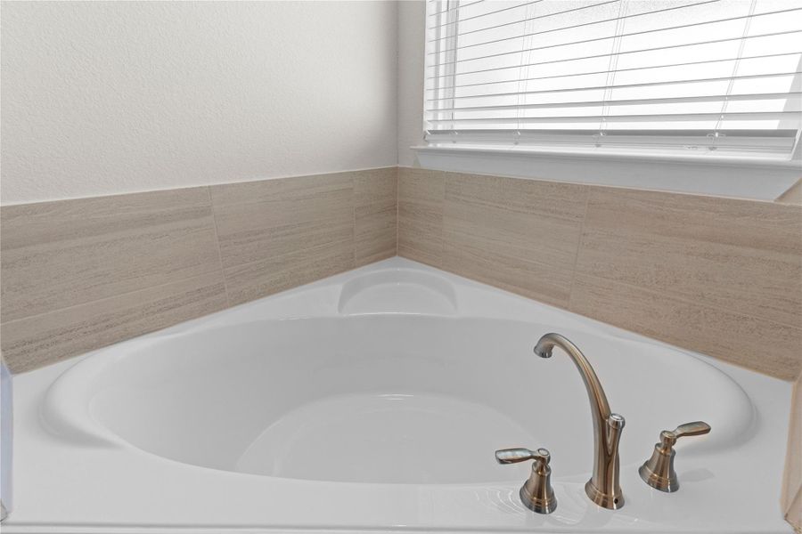 The soaking tub provides a relaxing focal point in the primary bath, surrounded by tasteful tile accents and natural light, offering a peaceful escape that completes this inviting primary suite.