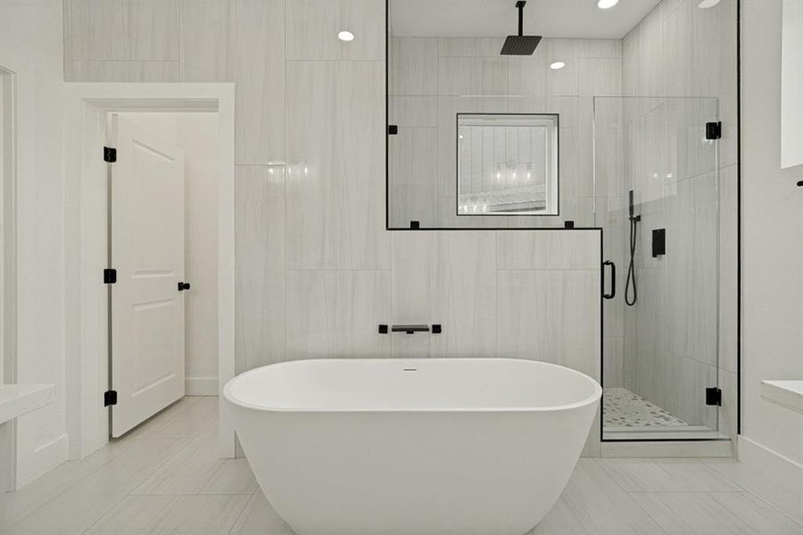 Freestanding soaking tub centered in a bathroom featuring light-toned large format tile flooring and wall finishes Freestanding soaking tub centered in a bathroom featuring light-toned large format tile flooring and wall finishes