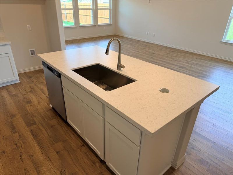 Kitchen island featuring a stainless steel undermount sink, gooseneck faucet, integrated dishwasher, and light-toned countertop