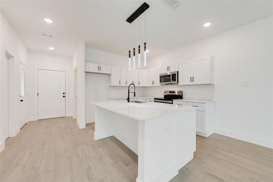 Kitchen with pendant lighting, stainless steel appliances, light countertops, a sink, and an island with sink