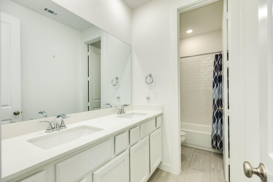 Secondary bathroom shared between the two secondary bedrooms, featuring double sinks, quartz countertops, a shower-tub combo, tile flooring, and ample storage space.