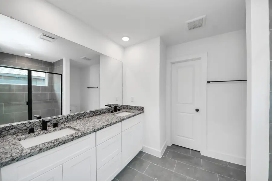 Primary Bathroom – Spacious primary bath featuring a dual-sink vanity with granite countertop, modern fixtures, large mirror, and a walk-in shower with contemporary tile surround.