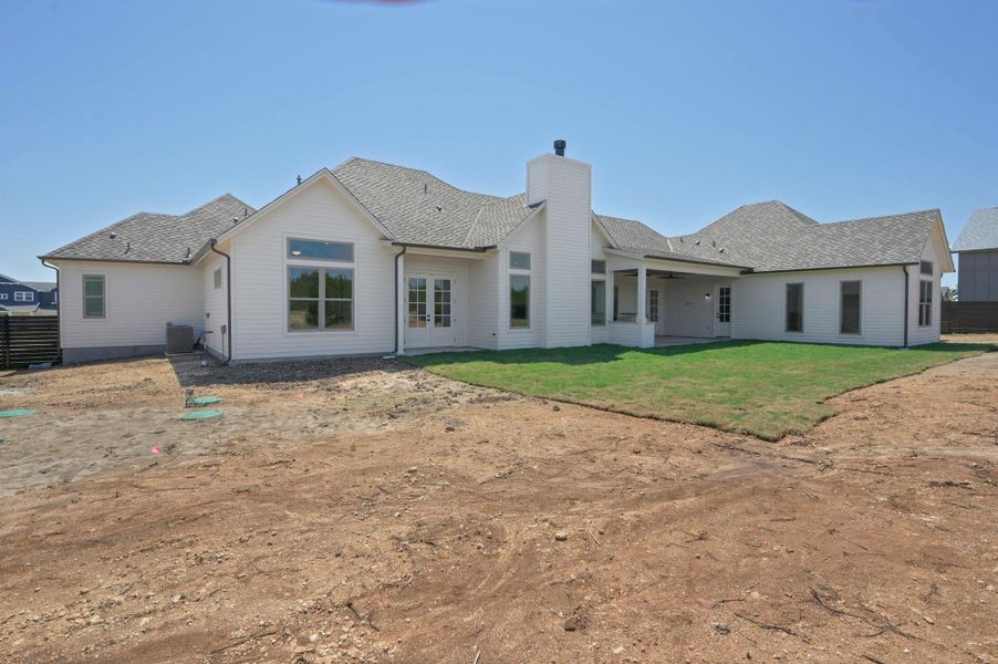 Back of property featuring a patio area, a chimney, a ceiling fan, a shingled roof, and a lawn