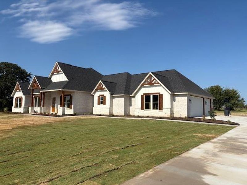 Modern farmhouse style home with a front yard, concrete driveway, covered porch, board and batten siding, and a garage