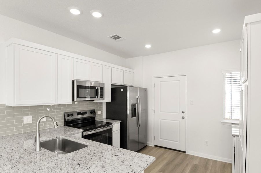 Kitchen with stainless steel appliances, light stone counters, white cabinets, backsplash, and recessed lighting