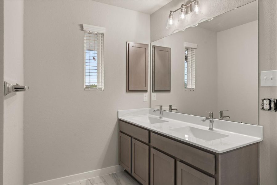 This bathroom features a sleek double vanity with modern fixtures, ample storage, and a large mirror. Two narrow windows provide natural light, complementing the clean and contemporary design.