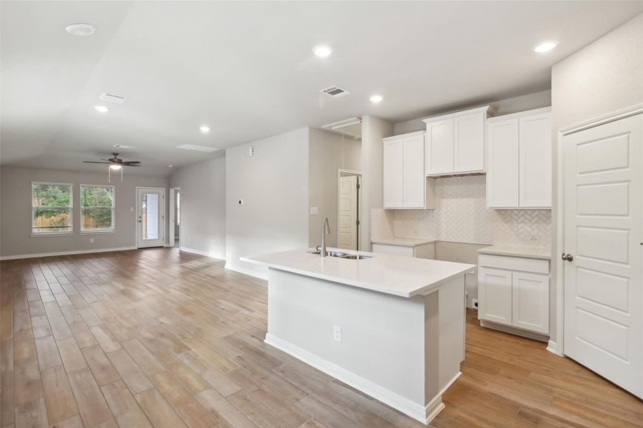 Kitchen featuring a sink, decorative backsplash, light wood finished floors, a kitchen island with sink, and white cabinetry Kitchen featuring a sink, decorative backsplash, light wood finished floors, a kitchen island with sink, and white cabinetry