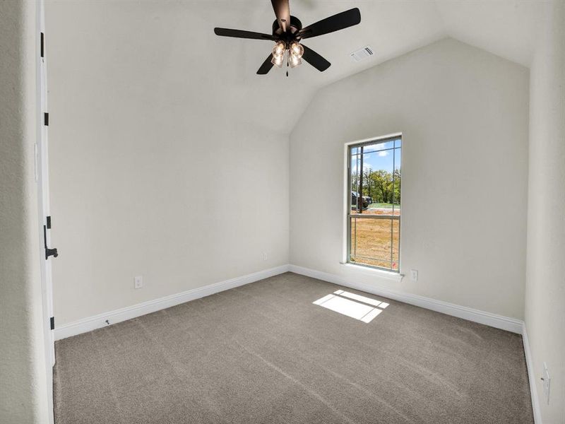 Carpeted empty room featuring baseboards, visible vents, ceiling fan, and lofted ceiling Carpeted empty room featuring baseboards, visible vents, ceiling fan, and lofted ceiling