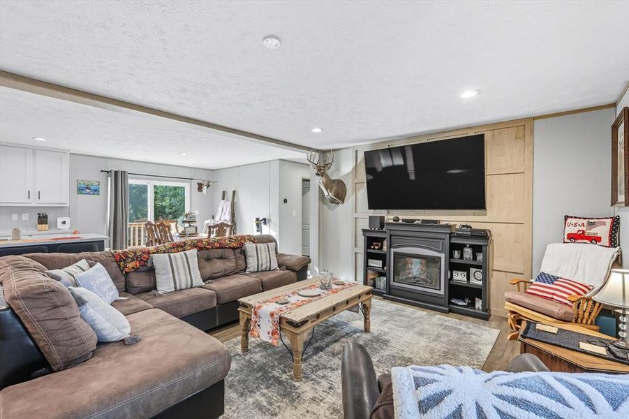Living room featuring recessed lighting, a glass covered fireplace, wood finished floors, and a textured ceiling Living room featuring recessed lighting, a glass covered fireplace, wood finished floors, and a textured ceiling