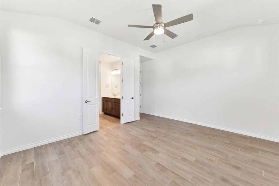 Unfurnished bedroom with baseboards, connected bathroom, visible vents, lofted ceiling, and light wood finished floors Unfurnished bedroom with baseboards, connected bathroom, visible vents, lofted ceiling, and light wood finished floors