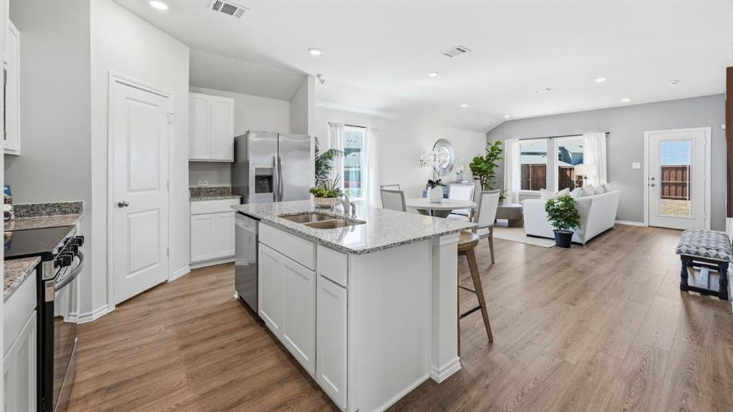Open concept living area featuring wood-look flooring, recessed lighting, and a kitchen with white cabinetry and granite countertops